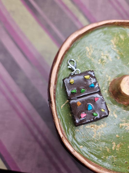 Brownie shaped charm with colorful dots on a green surface