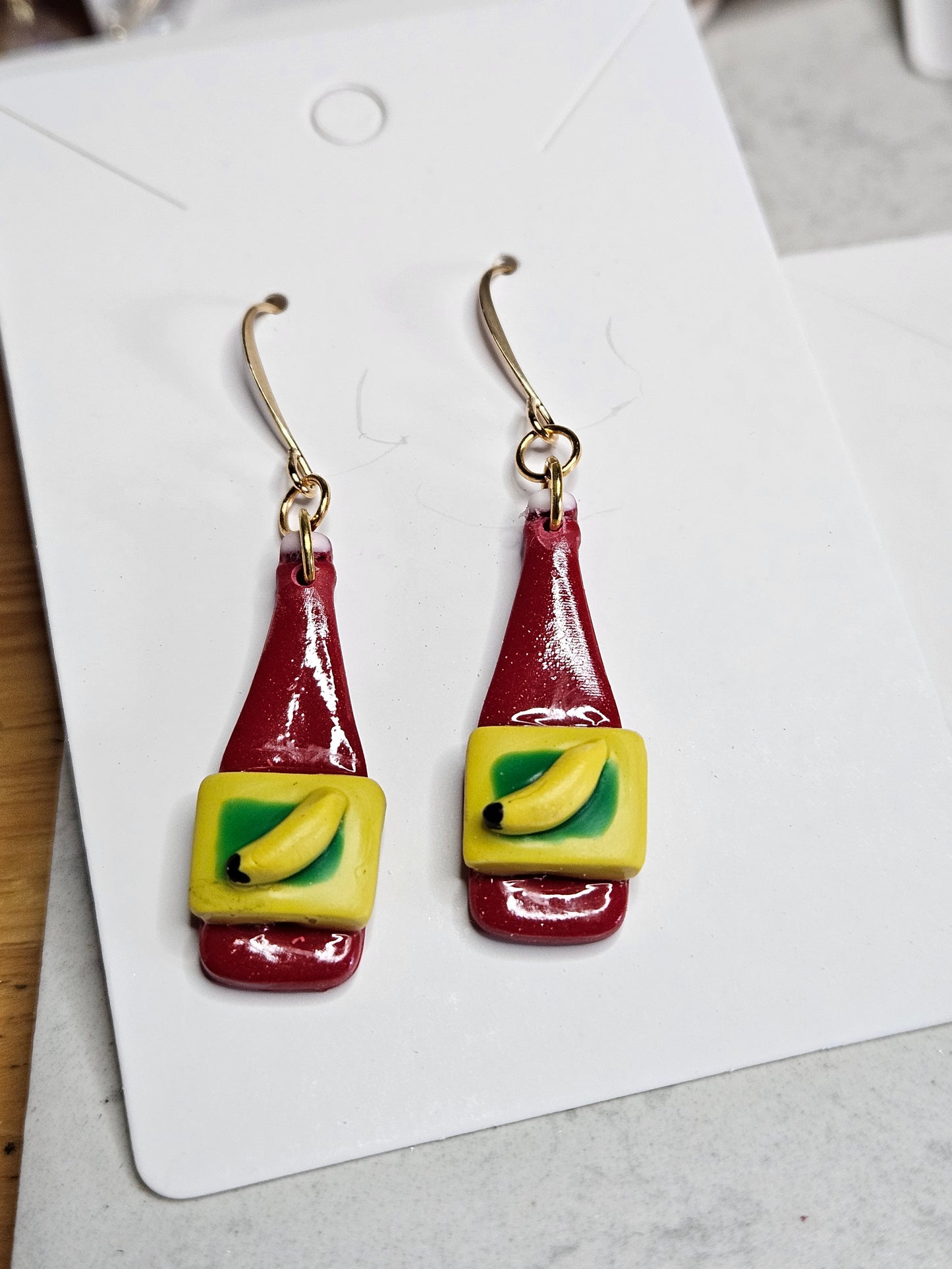 Pair of condiment bottle-shaped earrings on a white card with a gray background