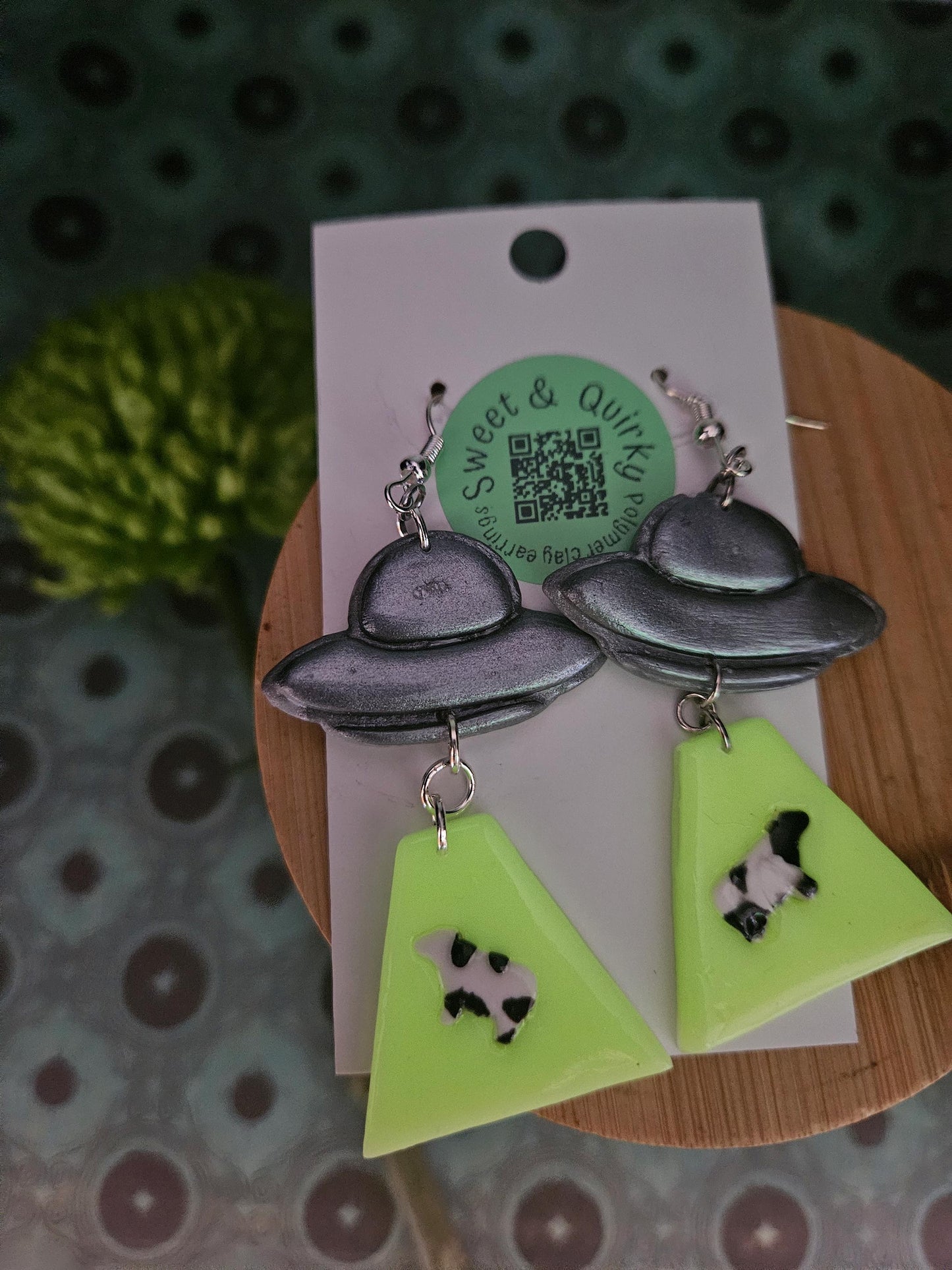 Earrings with UFO and triangle designs on a Sweet & Quirky branded card.