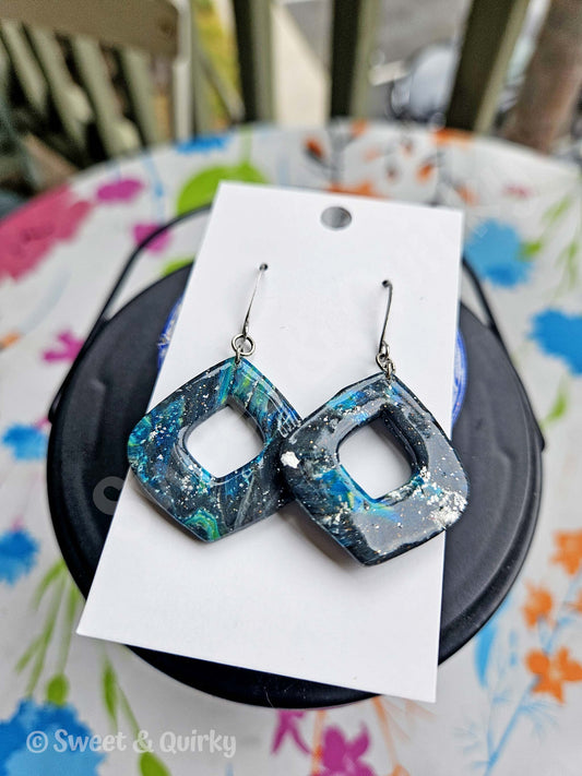 Blue and gray earrings on a white card placed on a colorful surface.