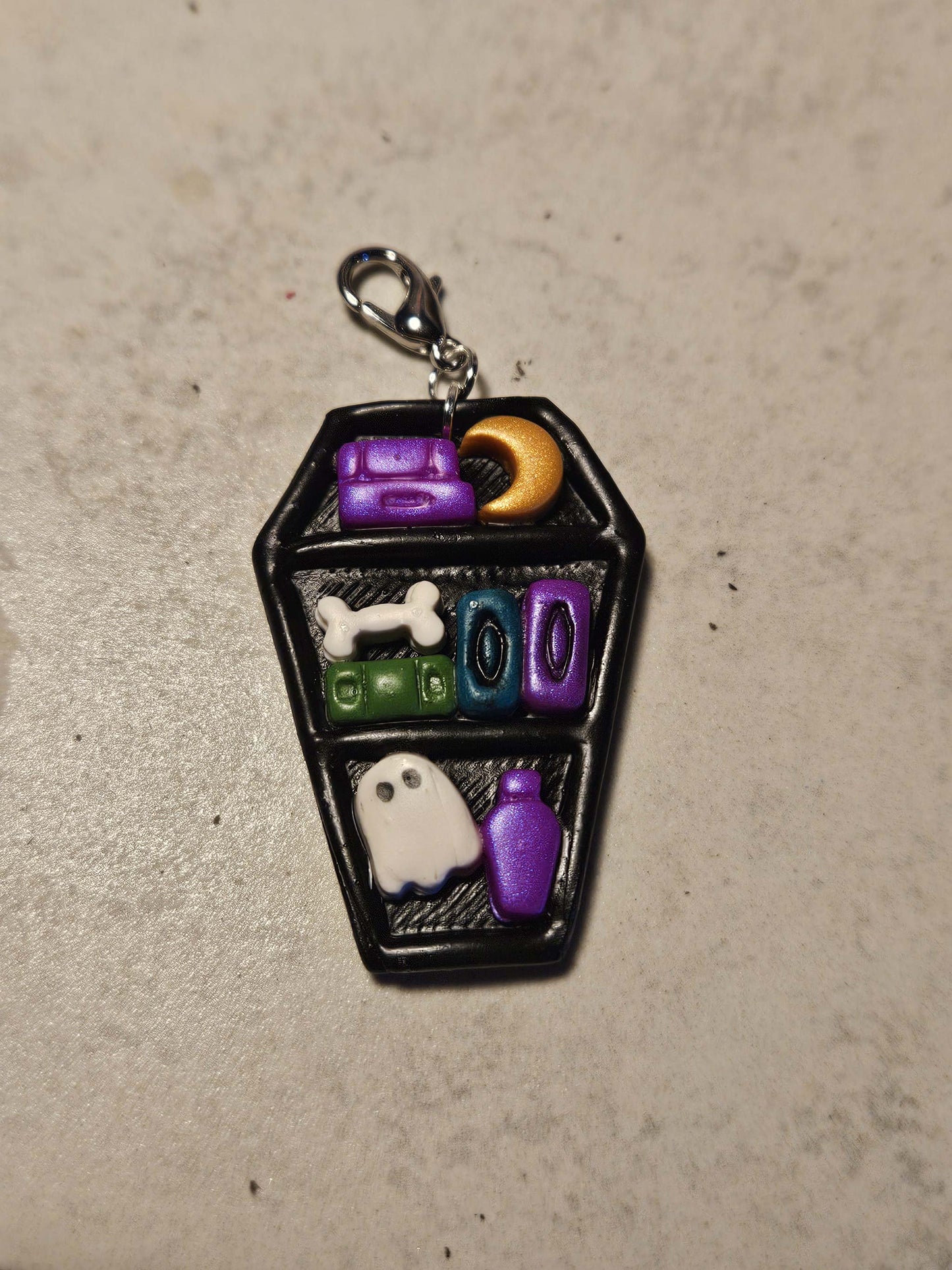 Decorative keychain shaped like a coffin with Halloween-themed elements on a beige surface.