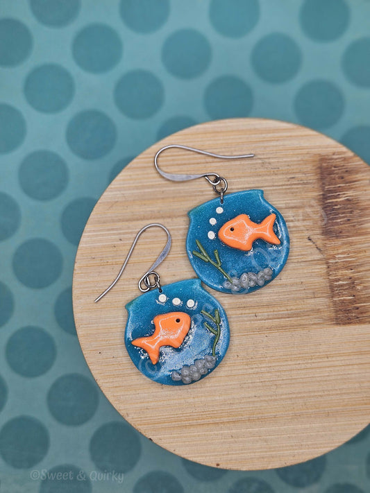 Pair of fish-themed earrings on a wooden board with a polka dot background
