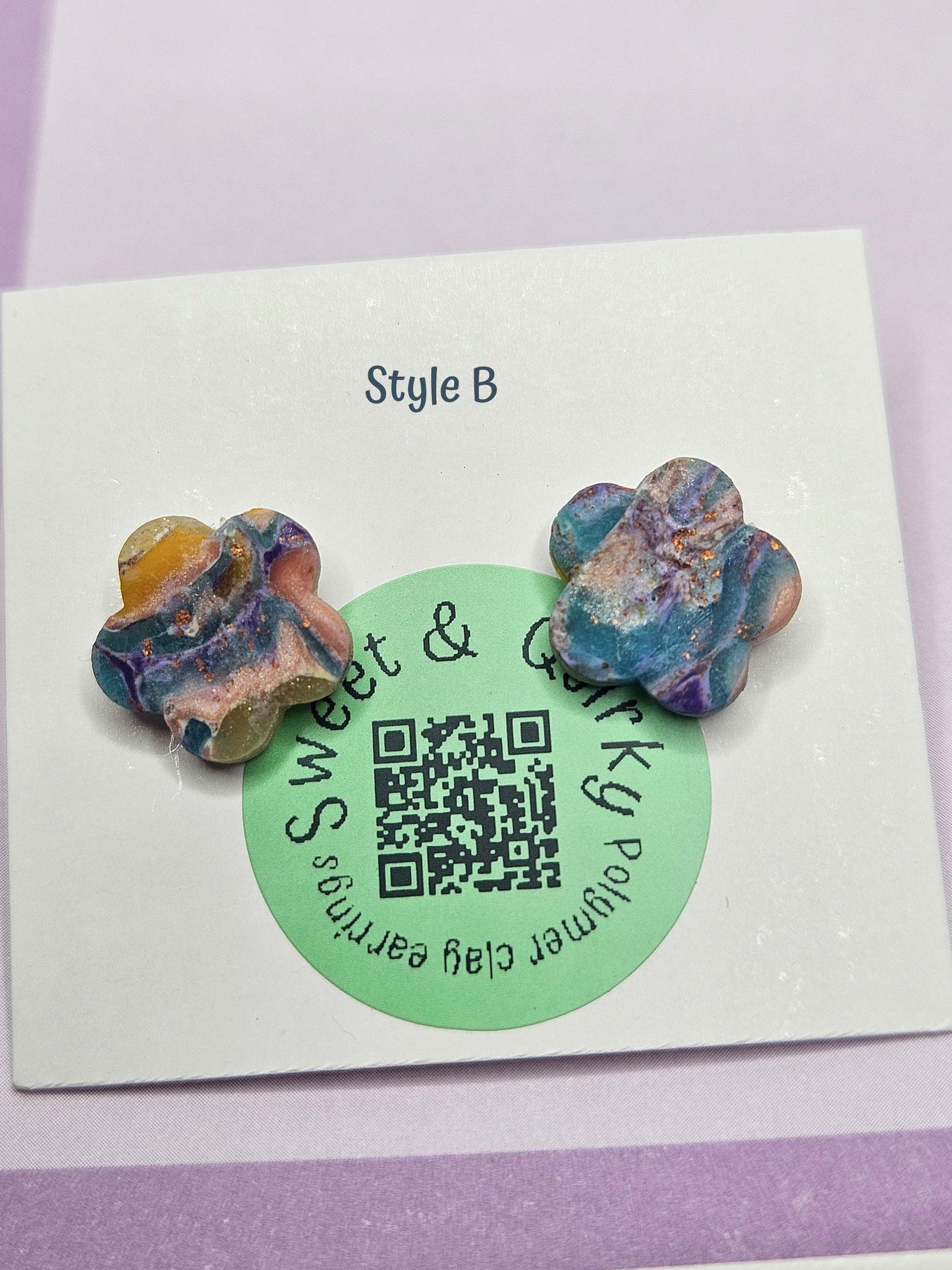 Pair of polymer clay earrings on a card with a QR code and brand name.