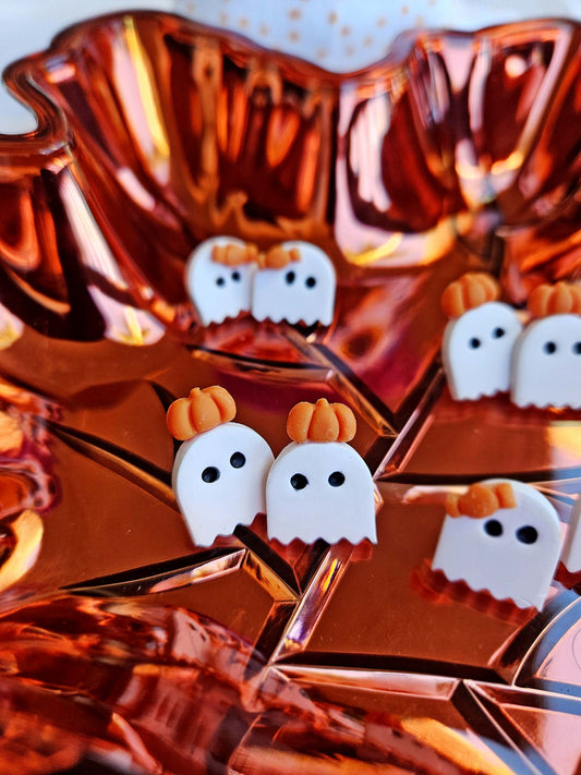 Halloween-themed earrings with ghost and pumpkin designs on a reflective surface.