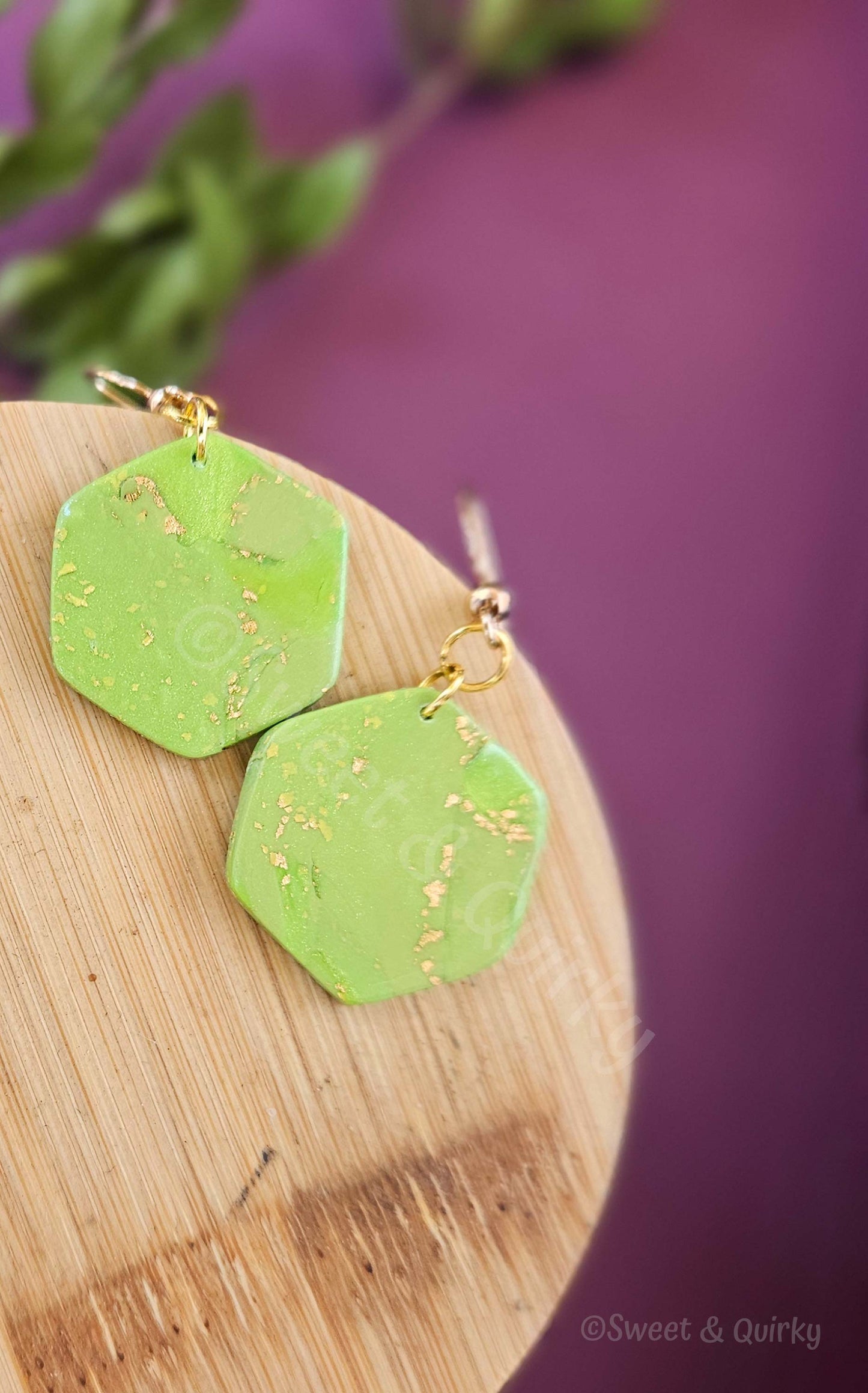 Green earrings with gold accents on a wooden board against a purple background