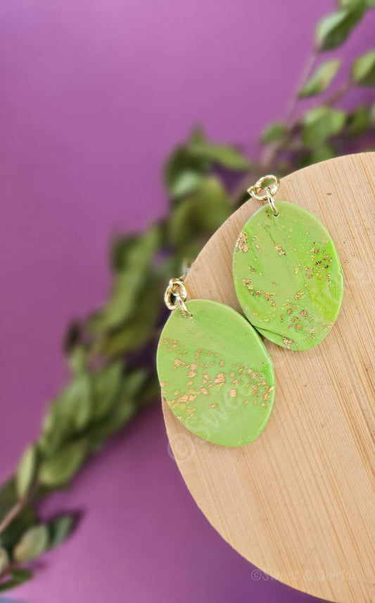 Green earrings with gold accents on a wooden board against a purple background
