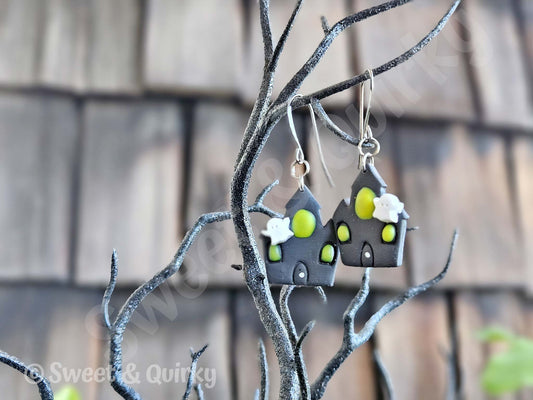 House-shaped earrings with green accents hanging on a branch.