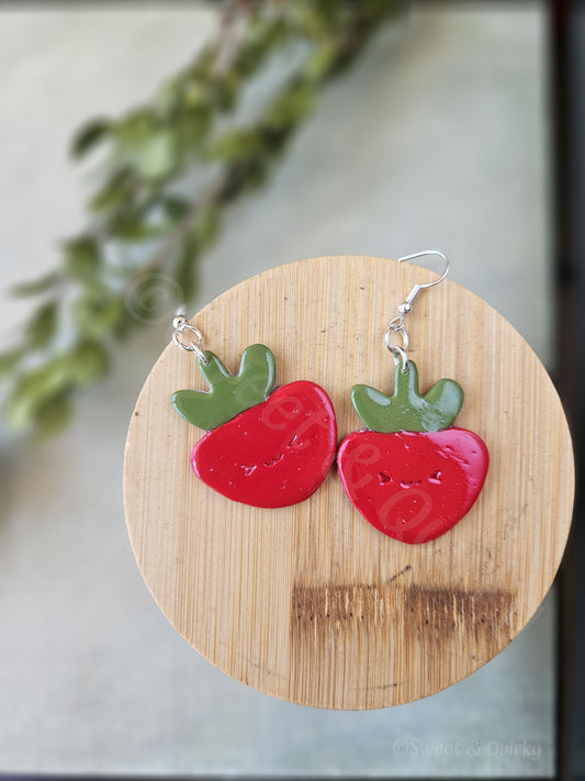 Strawberry-shaped earrings on a wooden board with a blurred green leafy background