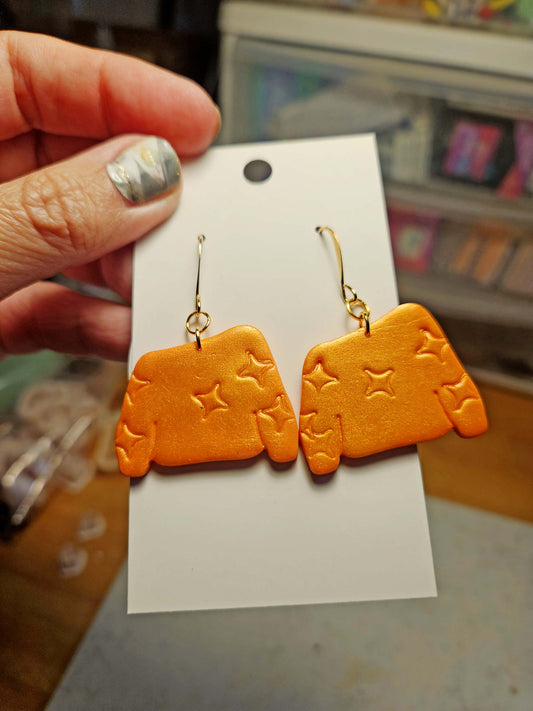 Orange sweater earrings with star designs on a white card held by a hand.