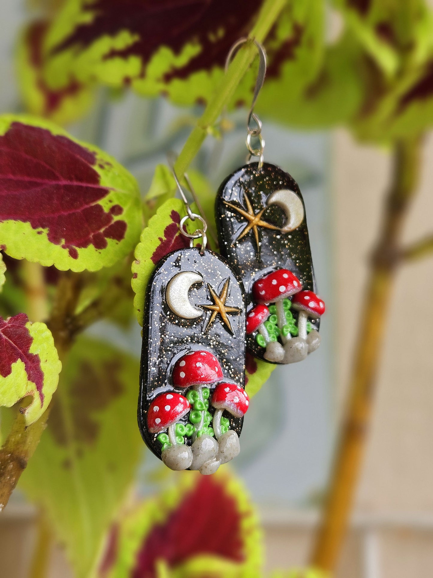 Pair of earrings with mushroom design hanging on a plant
