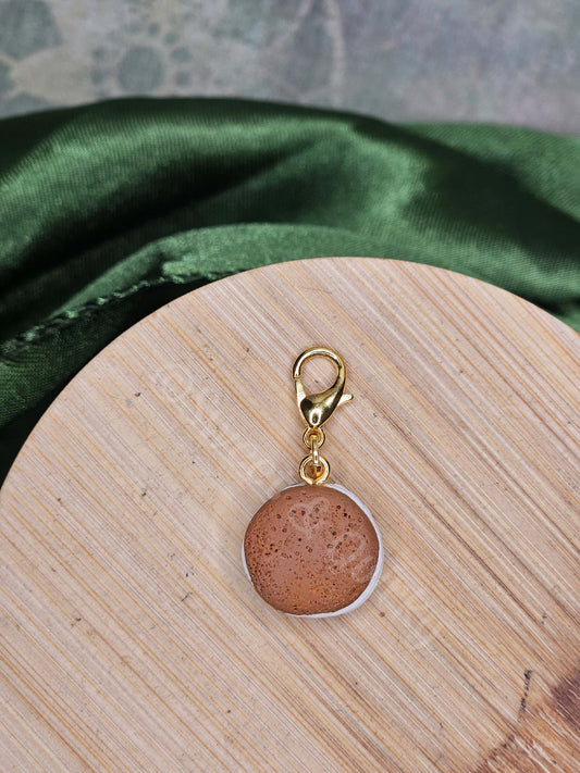 Pair of earrings on a wooden surface with a green fabric and pink geometric patterned background