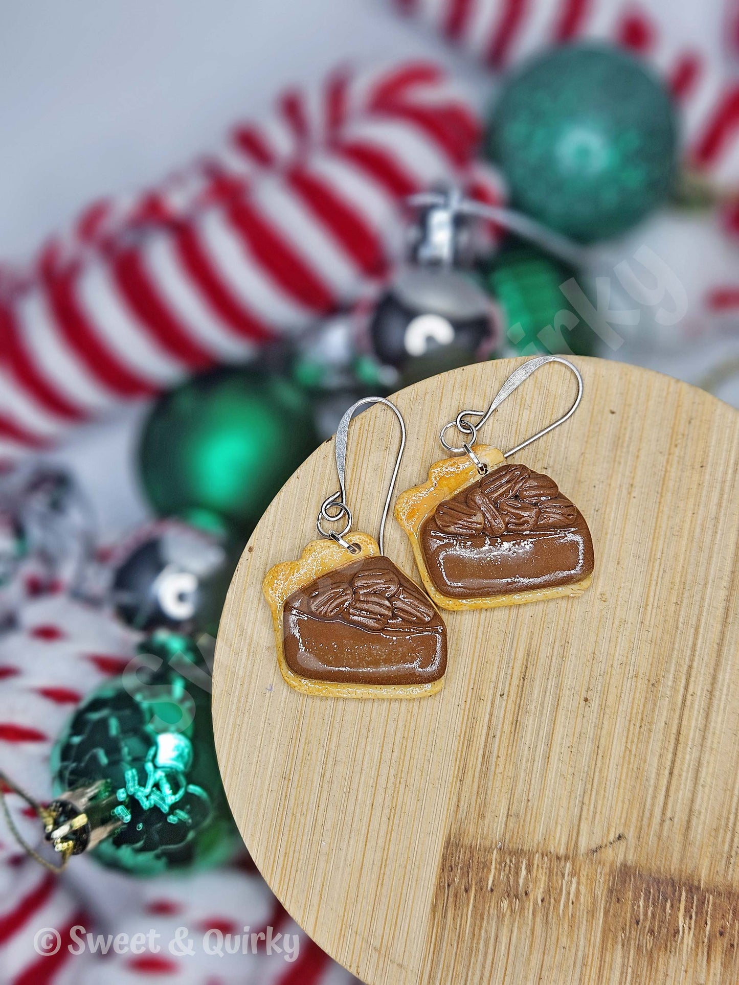 Earrings shaped like pecan pie on a wooden board, with Christmas decorations in the background.