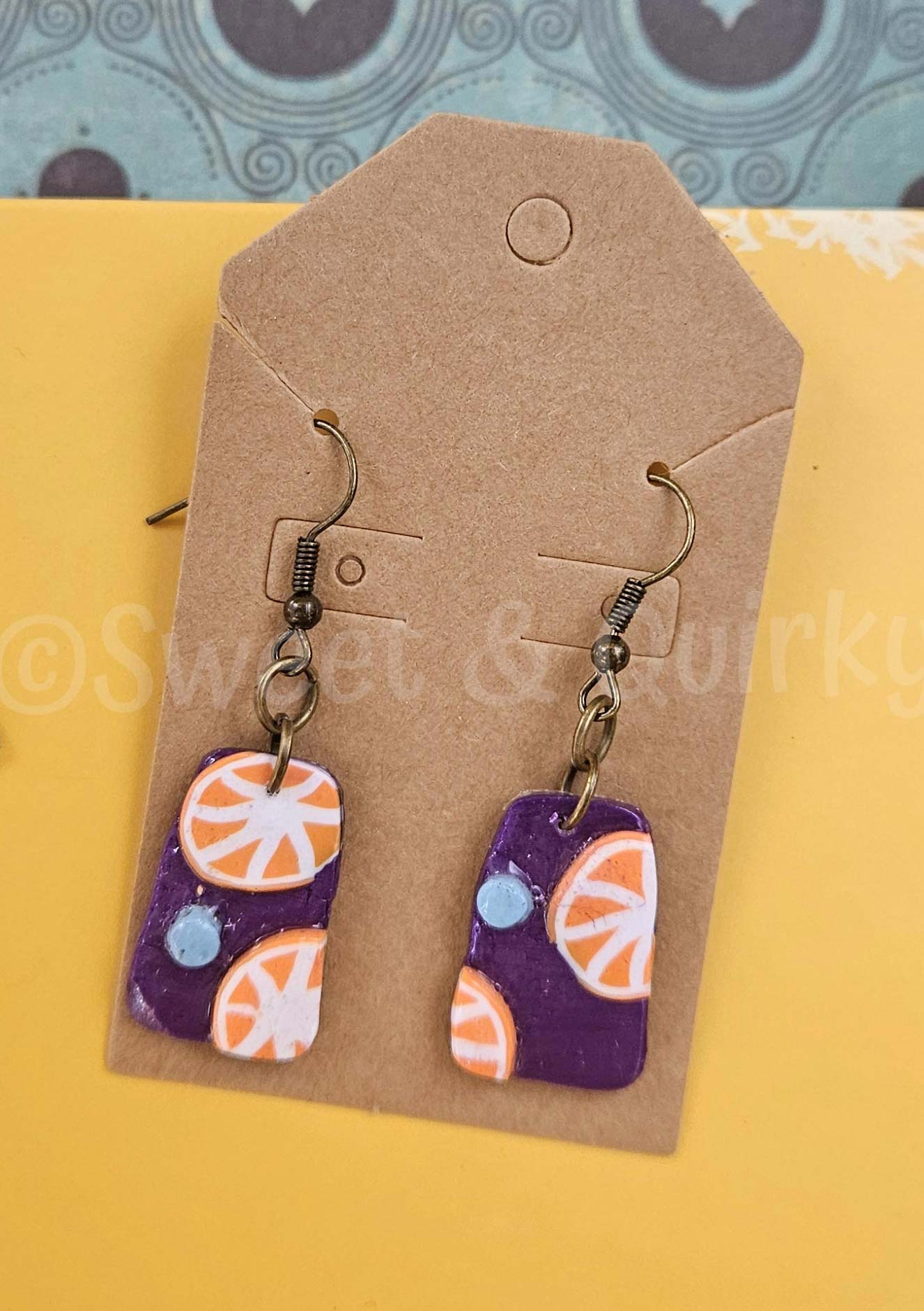 Pair of earrings with orange and purple design on a brown card with 'Sweet & Turkey' branding.