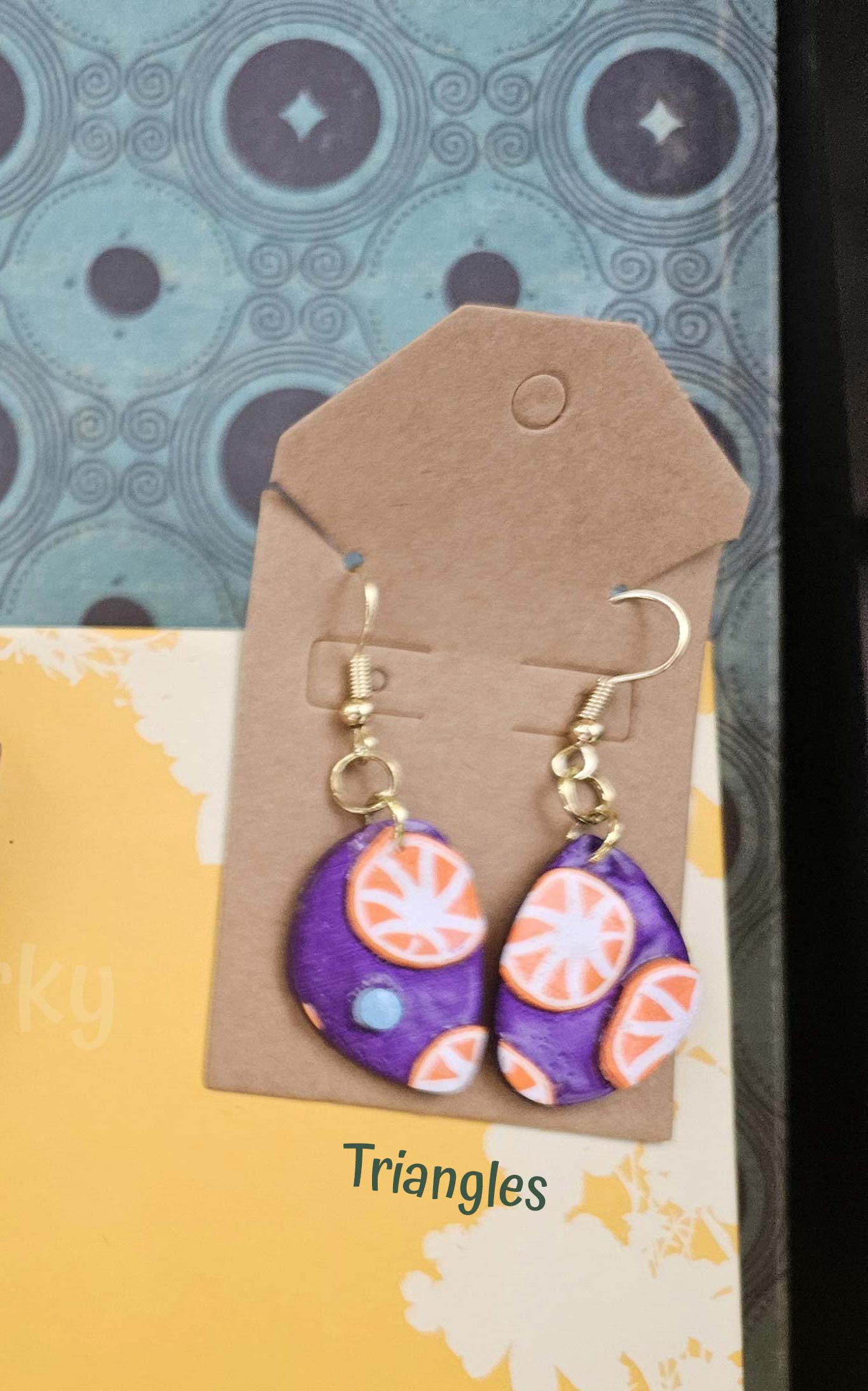 Pair of earrings with purple and orange design on a brown card with 'Triangles' text.