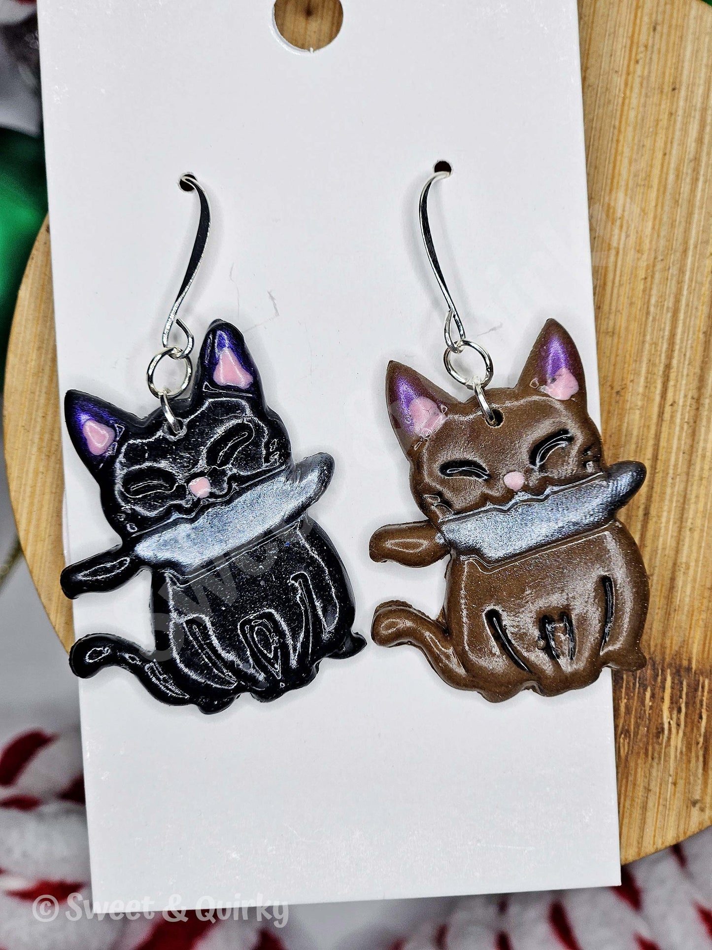 Pair of cat-shaped earrings on a white card with a wooden background