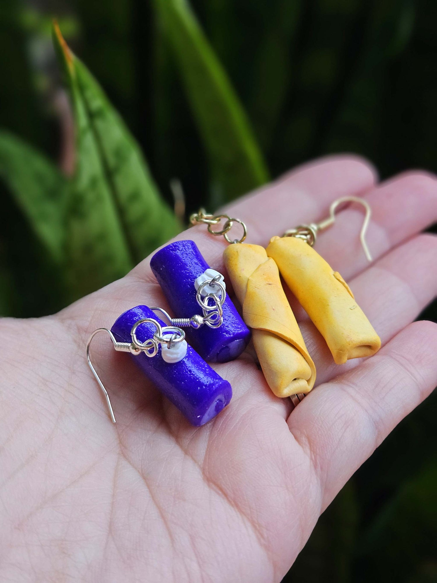 Purple and yellow earrings held in a hand with a blurred green background
