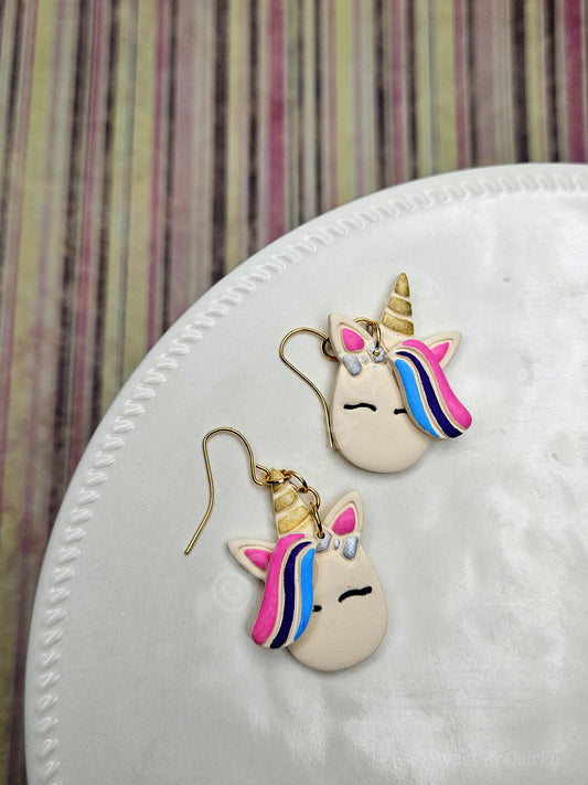 Unicorn-shaped earrings on a white surface with a striped background