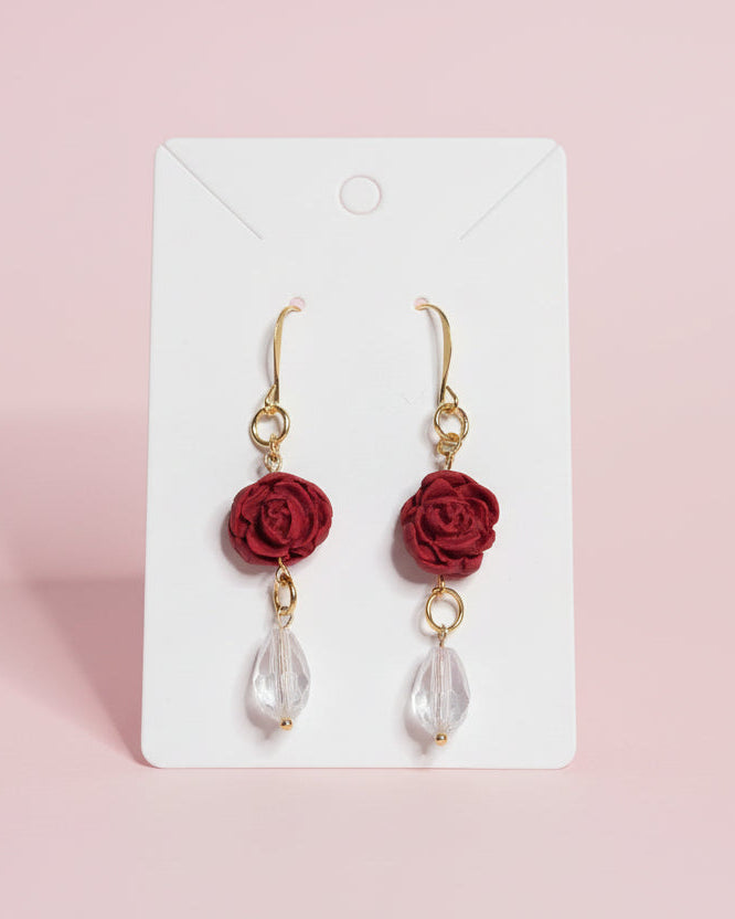 Pair of earrings with red rose and clear teardrop design on a white card.
