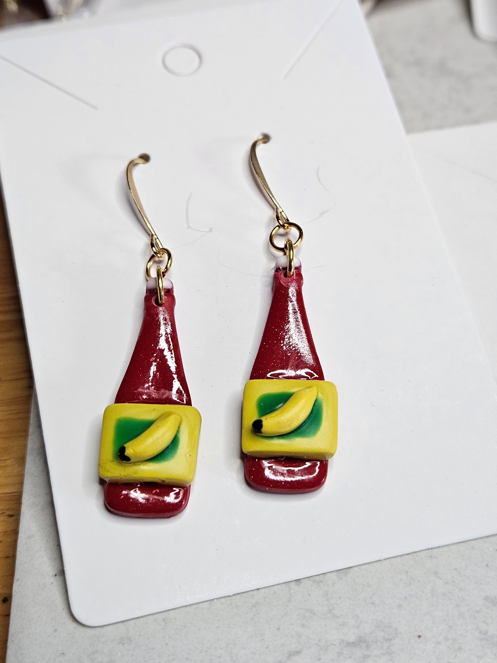 Pair of condiment bottle-shaped earrings on a white card with a gray background