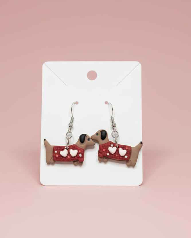 Dog-shaped earrings with red collars and white hearts on a white surface.