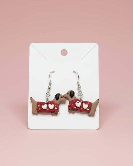 Dog-shaped earrings with red collars and white hearts on a white surface.