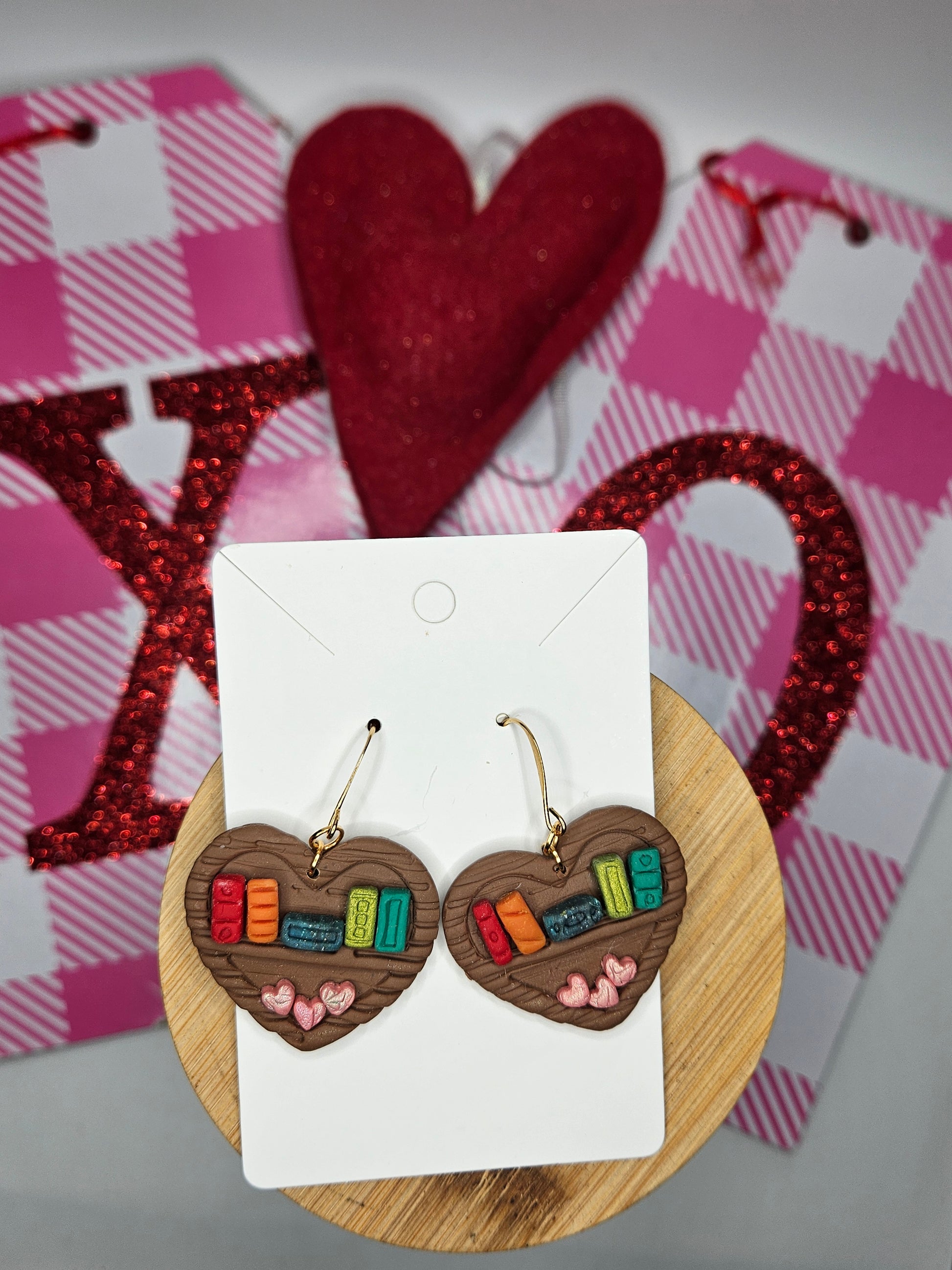 Wooden heart shaped bookshelf earrings on a card with red heart-shaped objects in the background