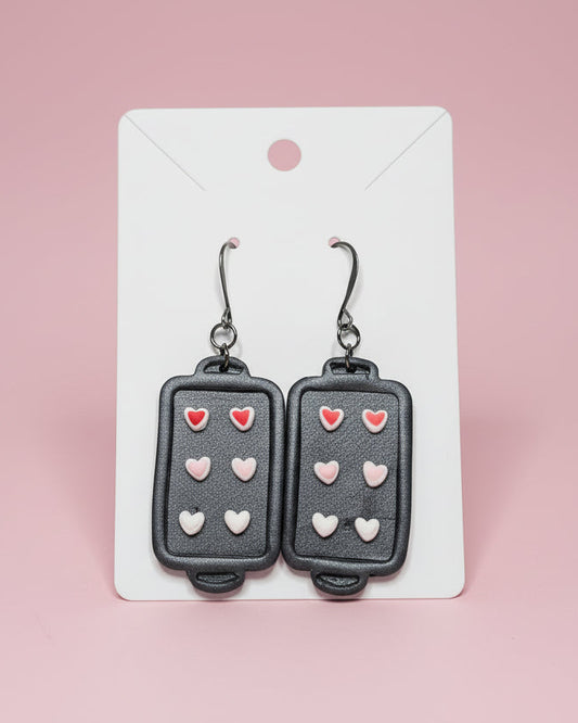 Earrings shaped like small baking sheets with heart sugar cookies on a white card.