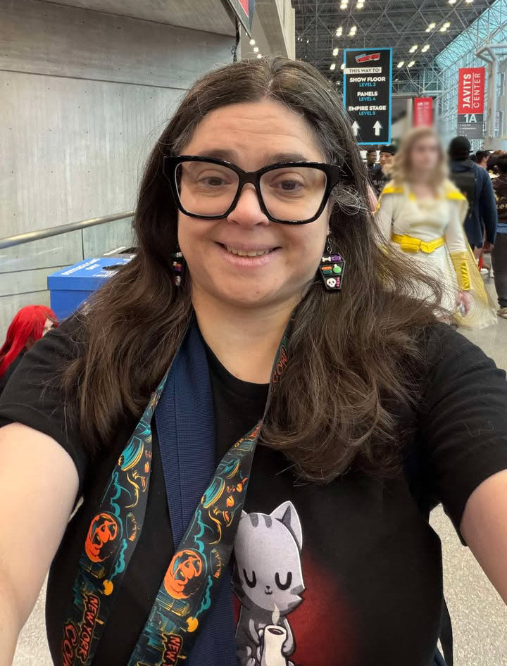 Woman wearing handmade polymer clay earrings shaped in the style of a coffin bookcase. Cute and quirky lightweight earrings worn at NY Comic Con!