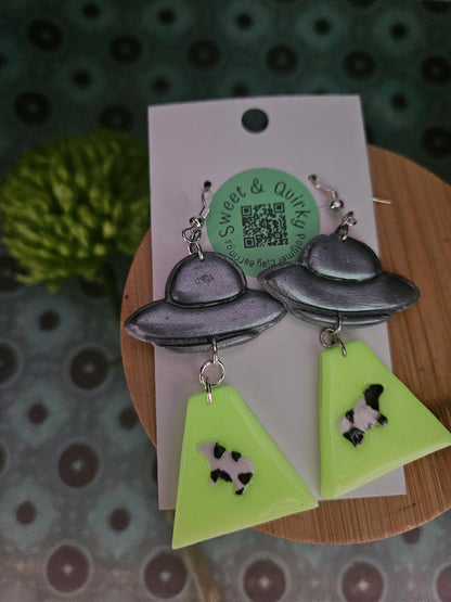 Earrings with UFO and triangle designs on a Sweet & Quirky branded card.