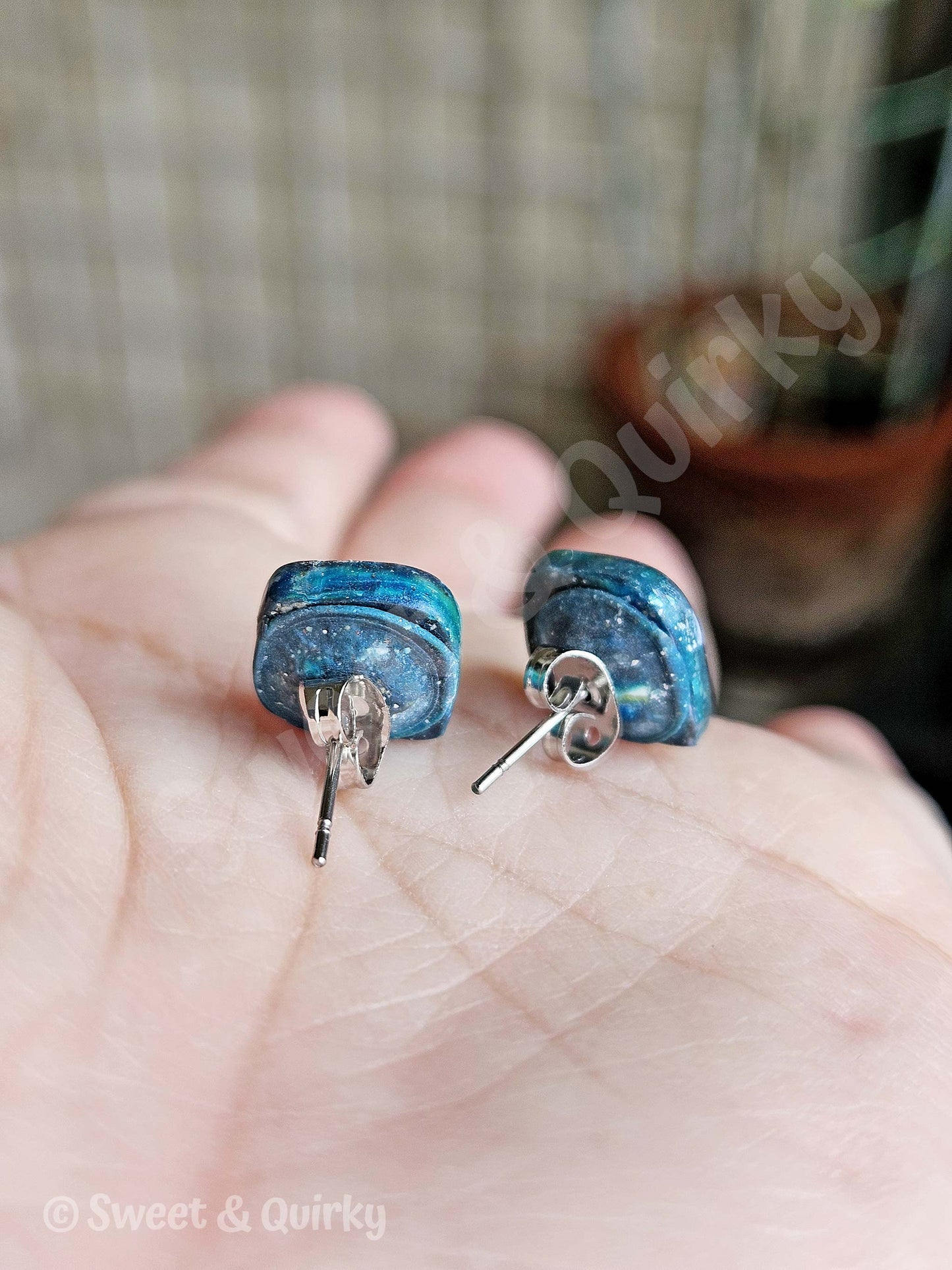 Blue earrings held in a hand with a blurred background