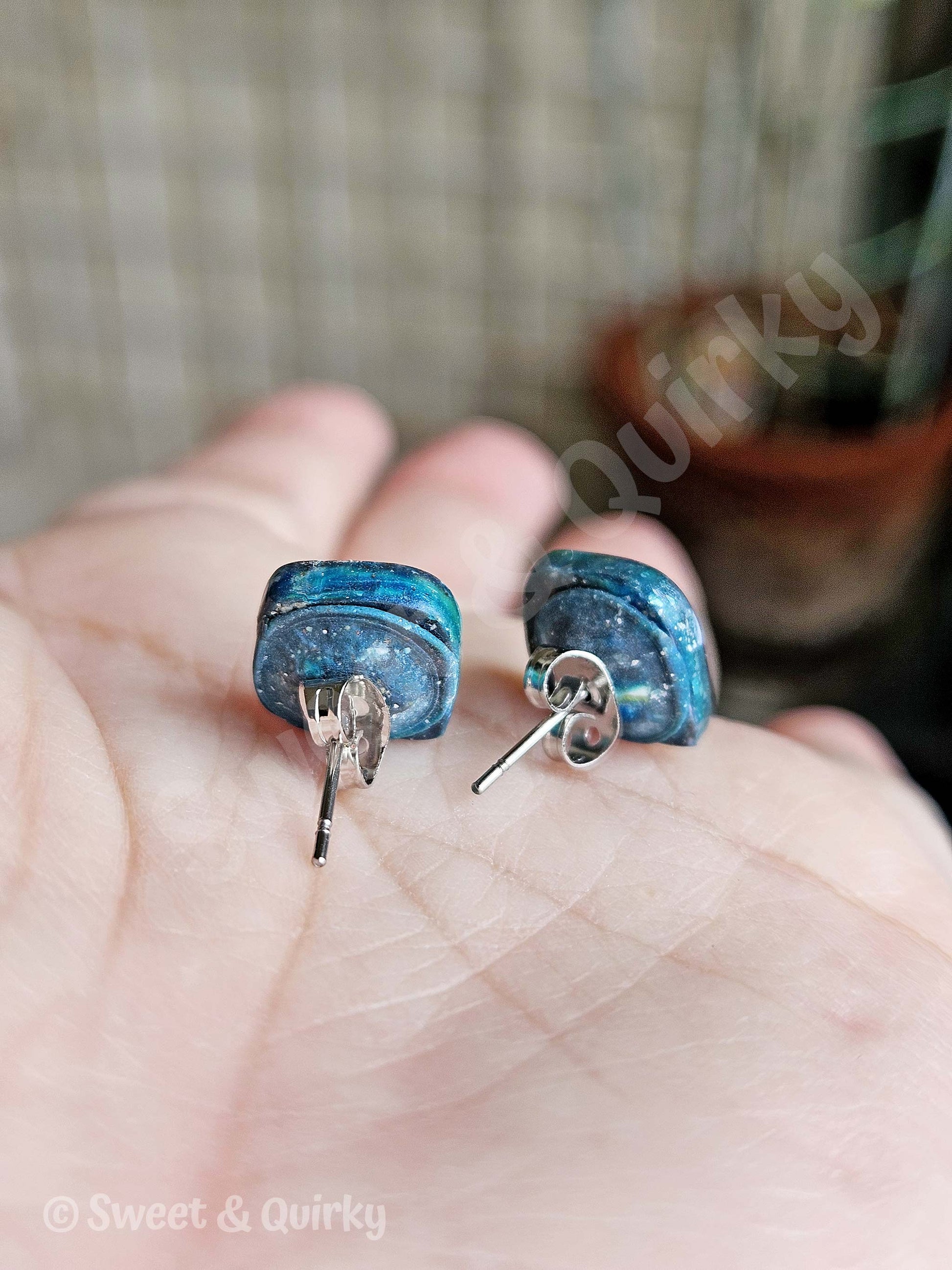 Blue earrings held in a hand with a blurred background