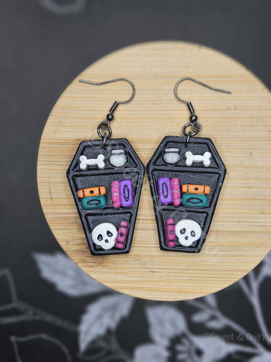 Pair of black coffin-shaped bookcase earrings with colorful designs on a wooden surface.
