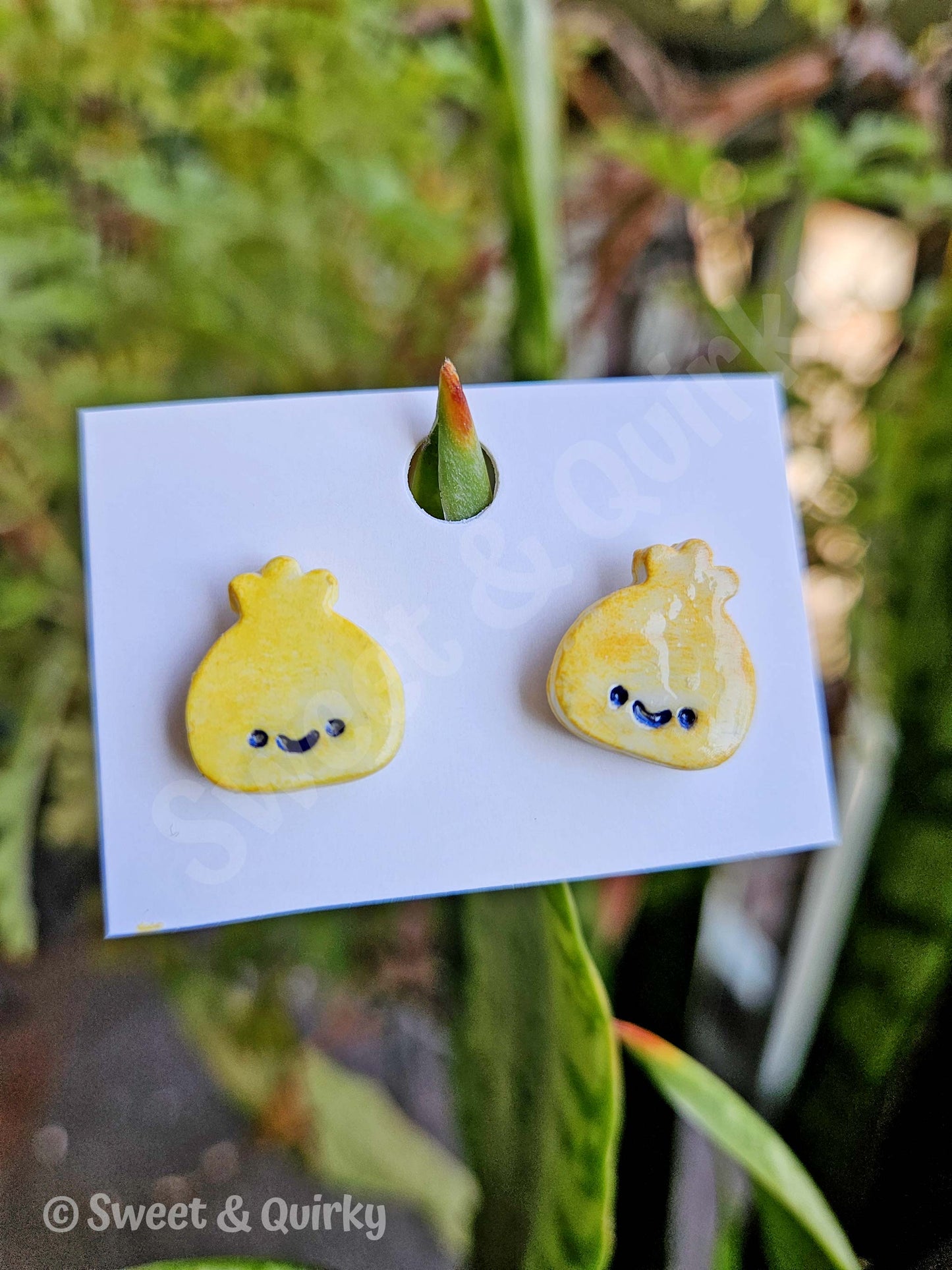 Yellow dumpling-shaped earrings on a display card with a blurred green plant background. Handmade in San Diego.