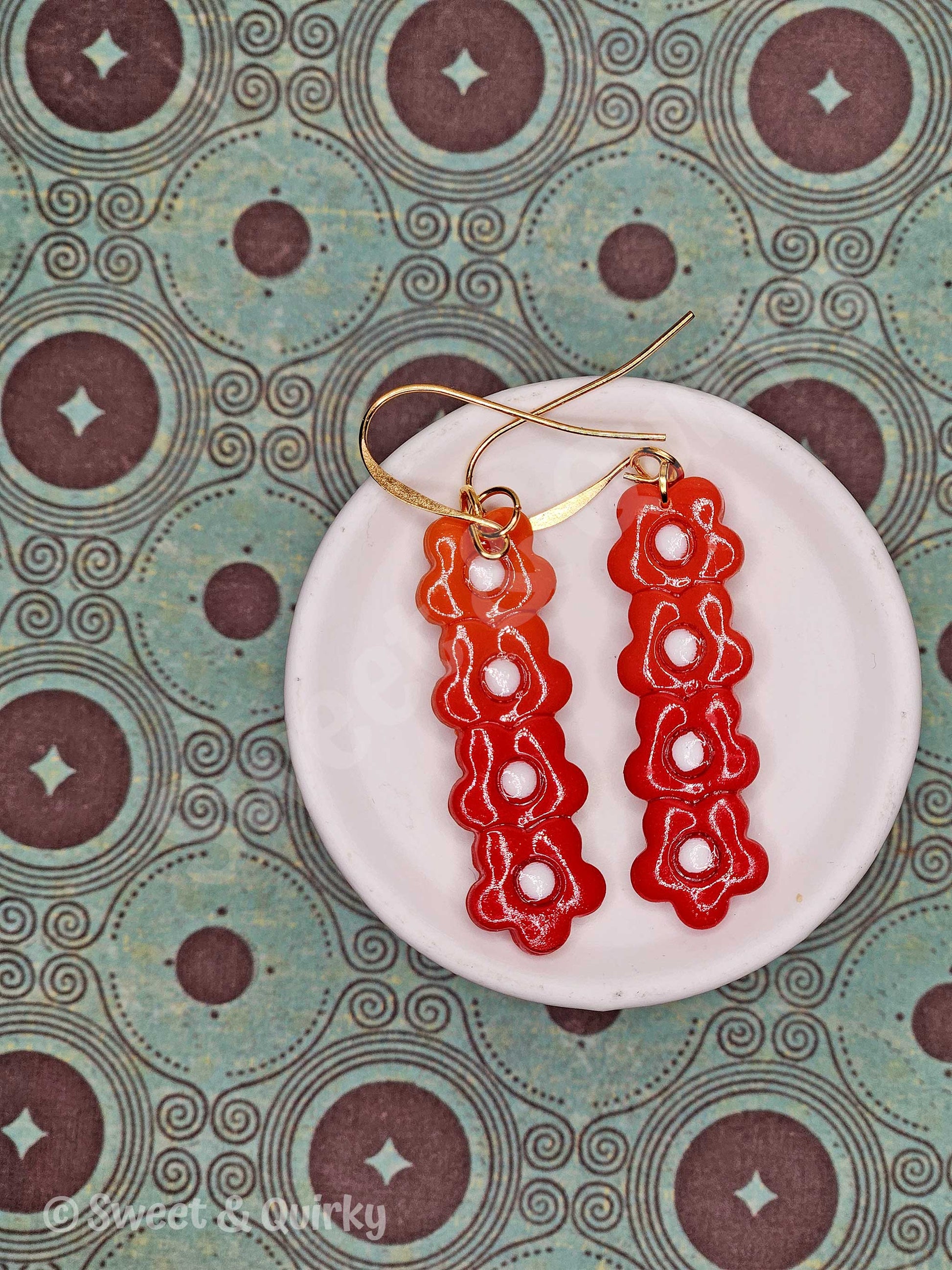 Red floral earrings on a white dish with a patterned background