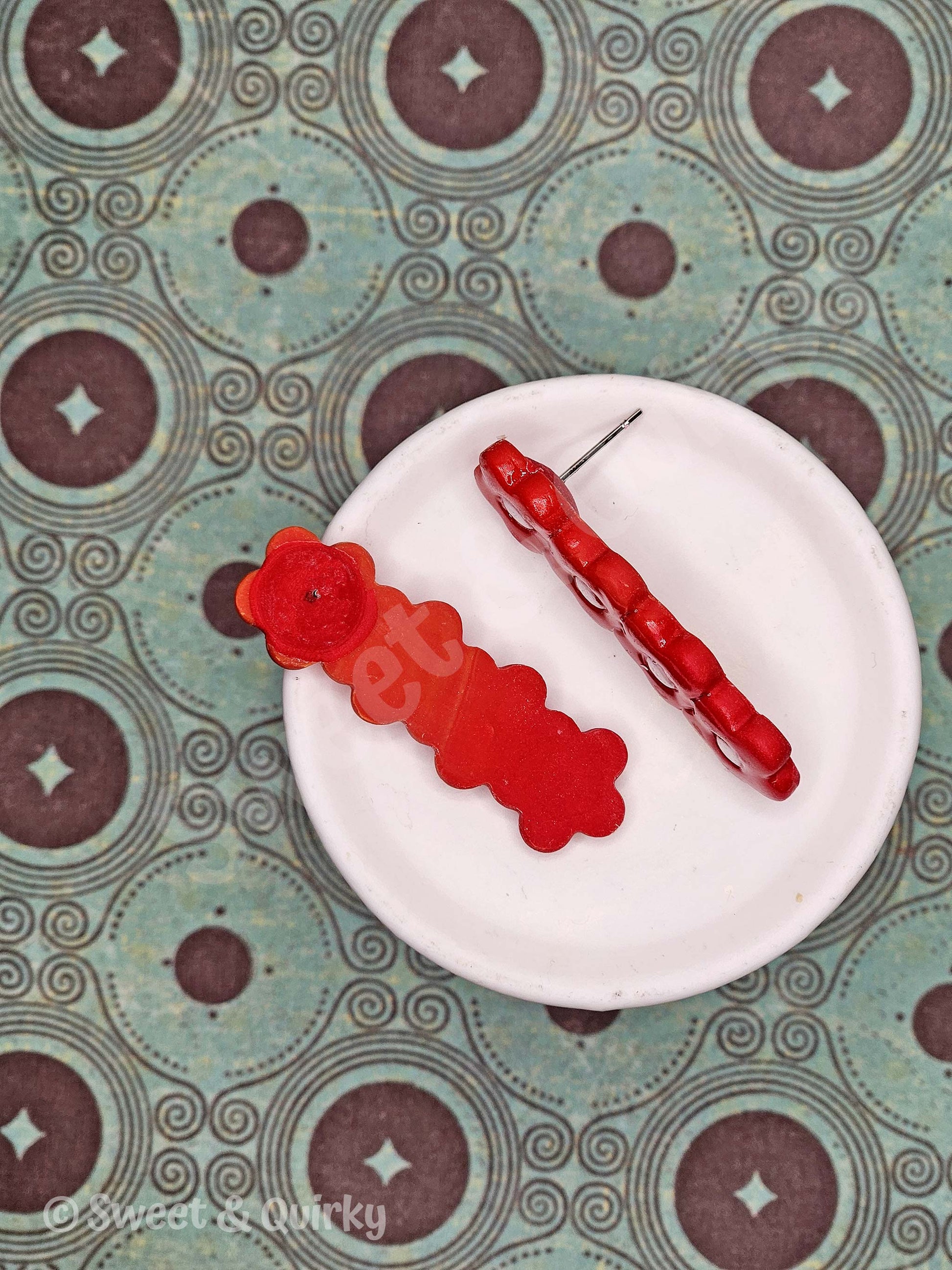 Red floral earring on a white plate with a patterned background