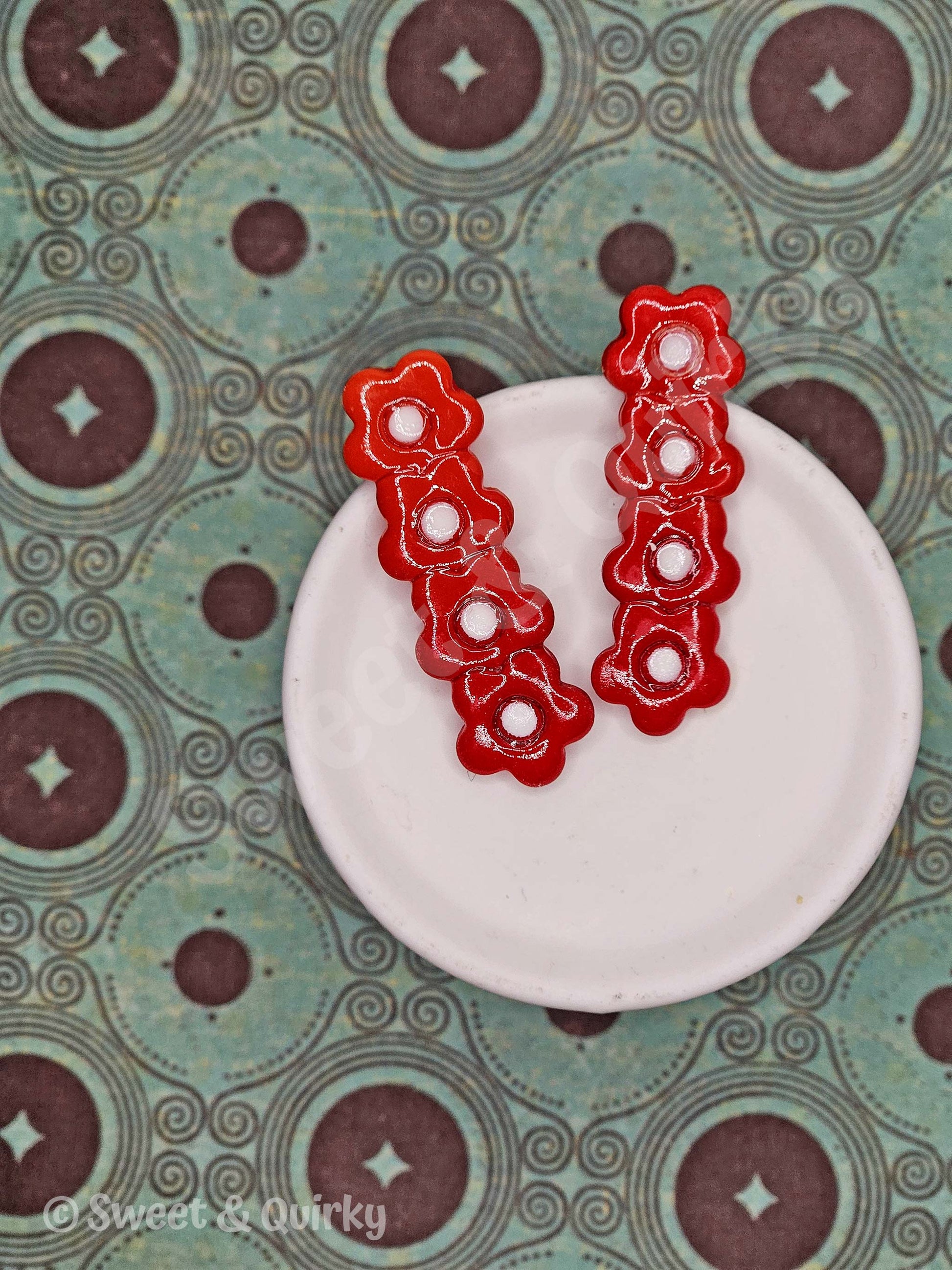 Red floral earrings on a white plate with a patterned background
