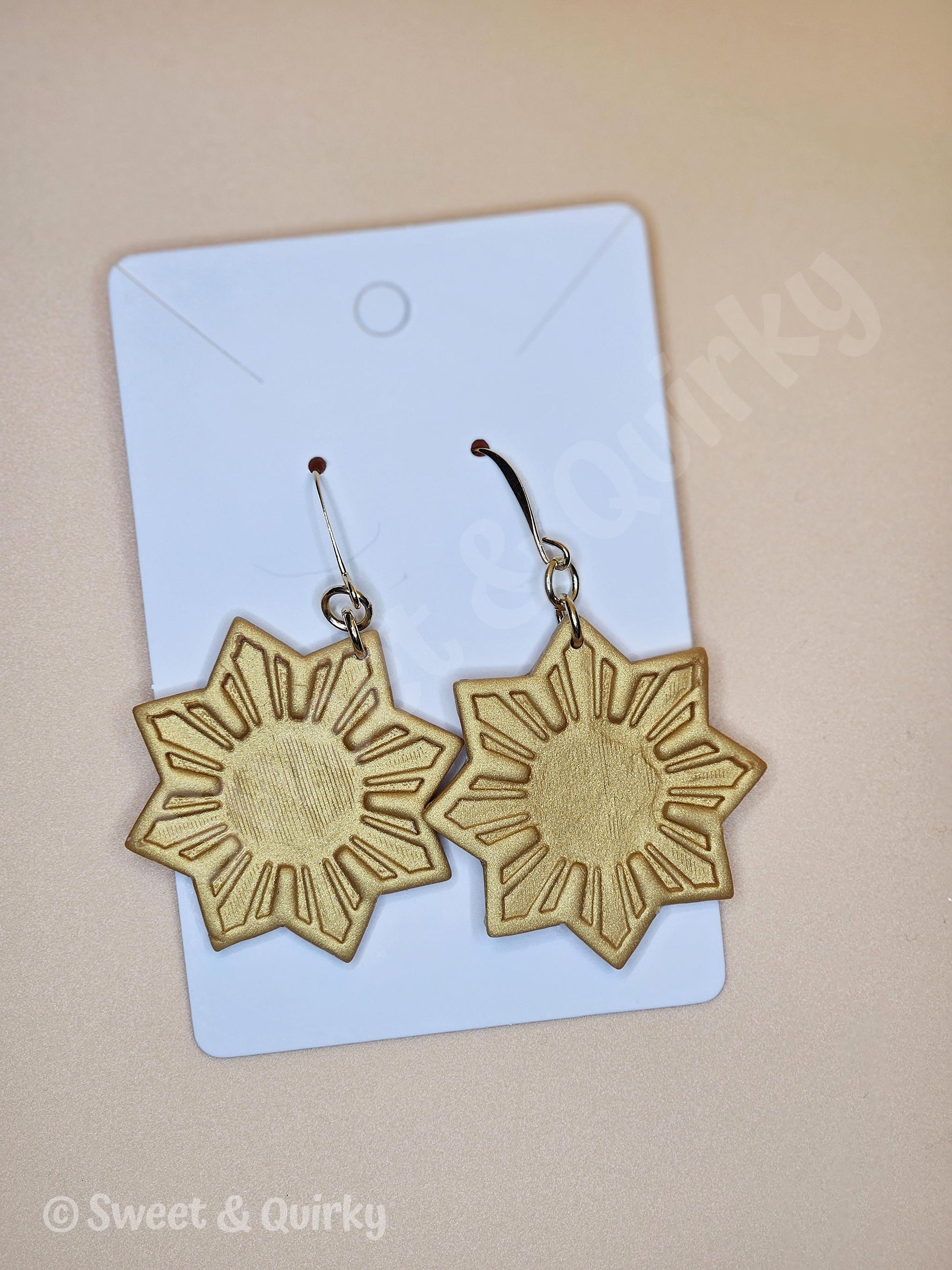 Gold sun-shaped earrings on a light blue card with 'Sweet & Quirky' branding.