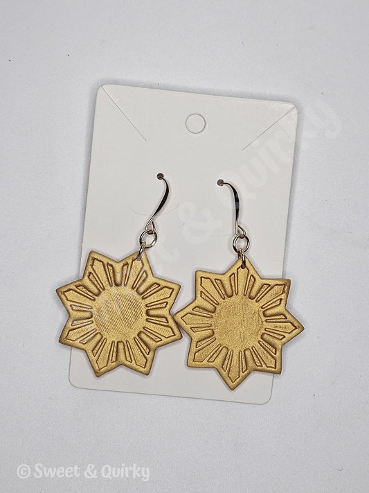Gold sun-shaped earrings on a clear card with 'Sweet & Quirky' branding.