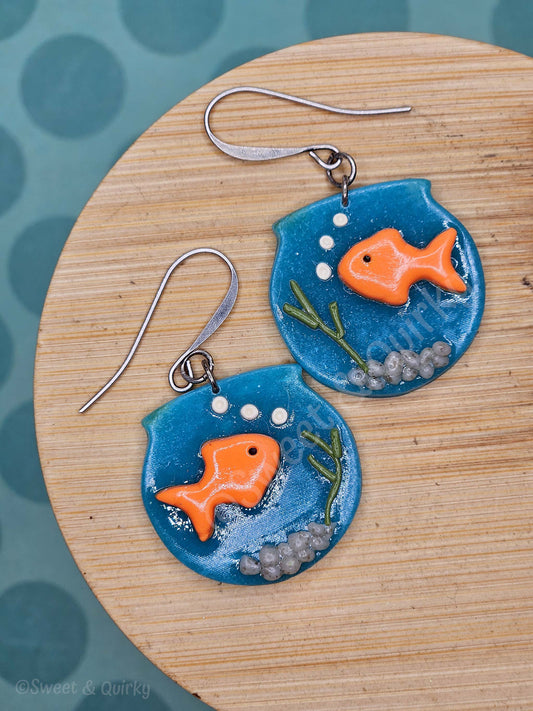 Pair of fish-themed earrings on a wooden board with a blue background