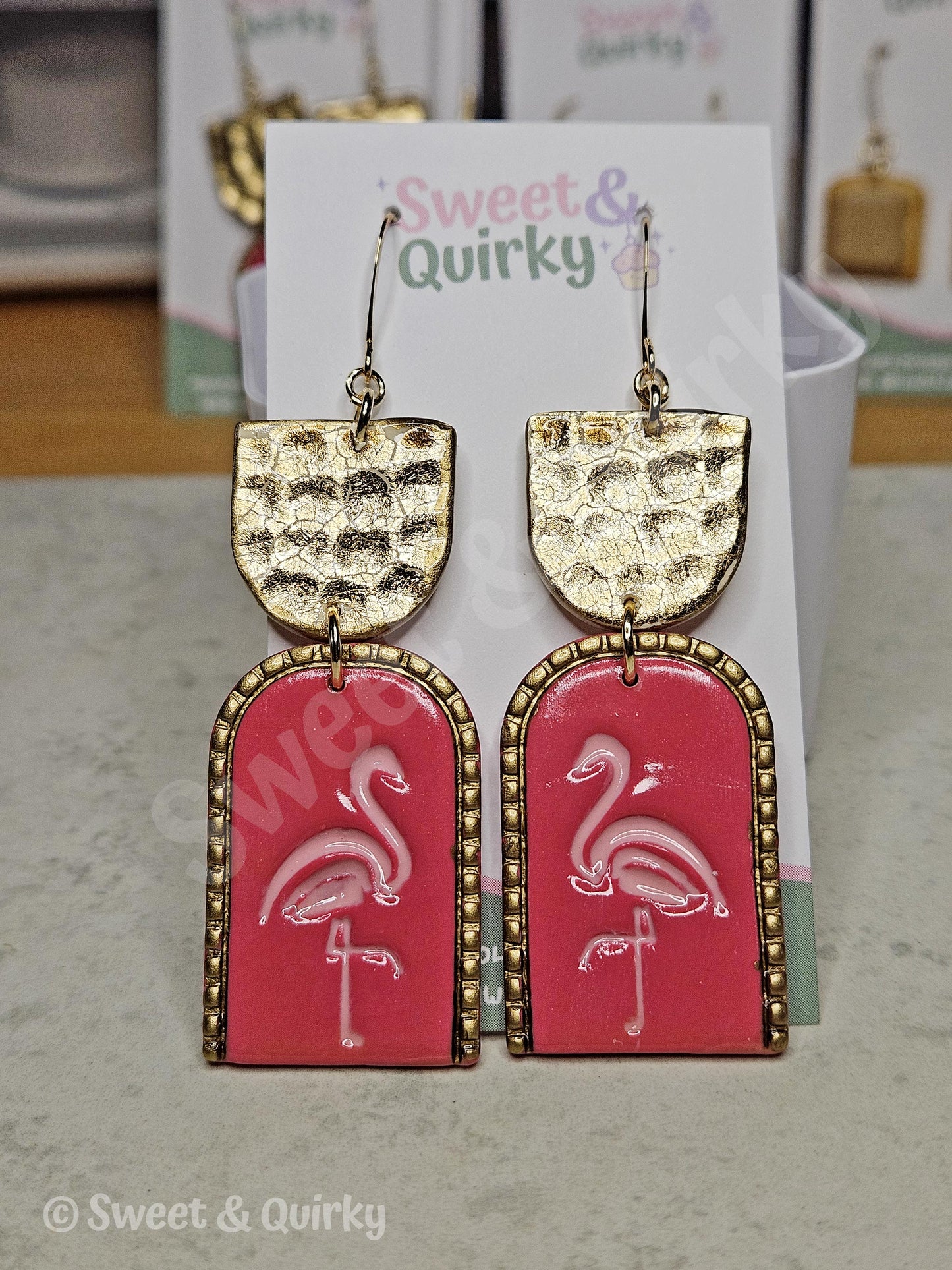 Pink flamingo earrings with gold accents on a Sweet & Quirky branded card.