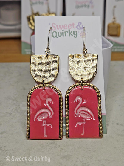 Pink flamingo earrings with gold accents on a Sweet & Quirky branded card.