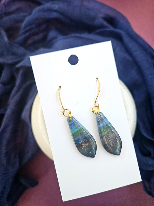 Teardrop-shaped earrings on a white card with a blue fabric background