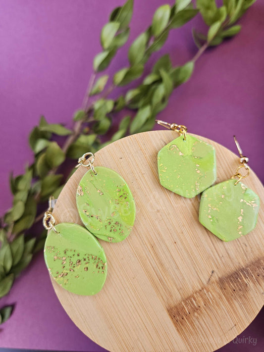 Green earrings with gold accents on a wooden board against a purple background