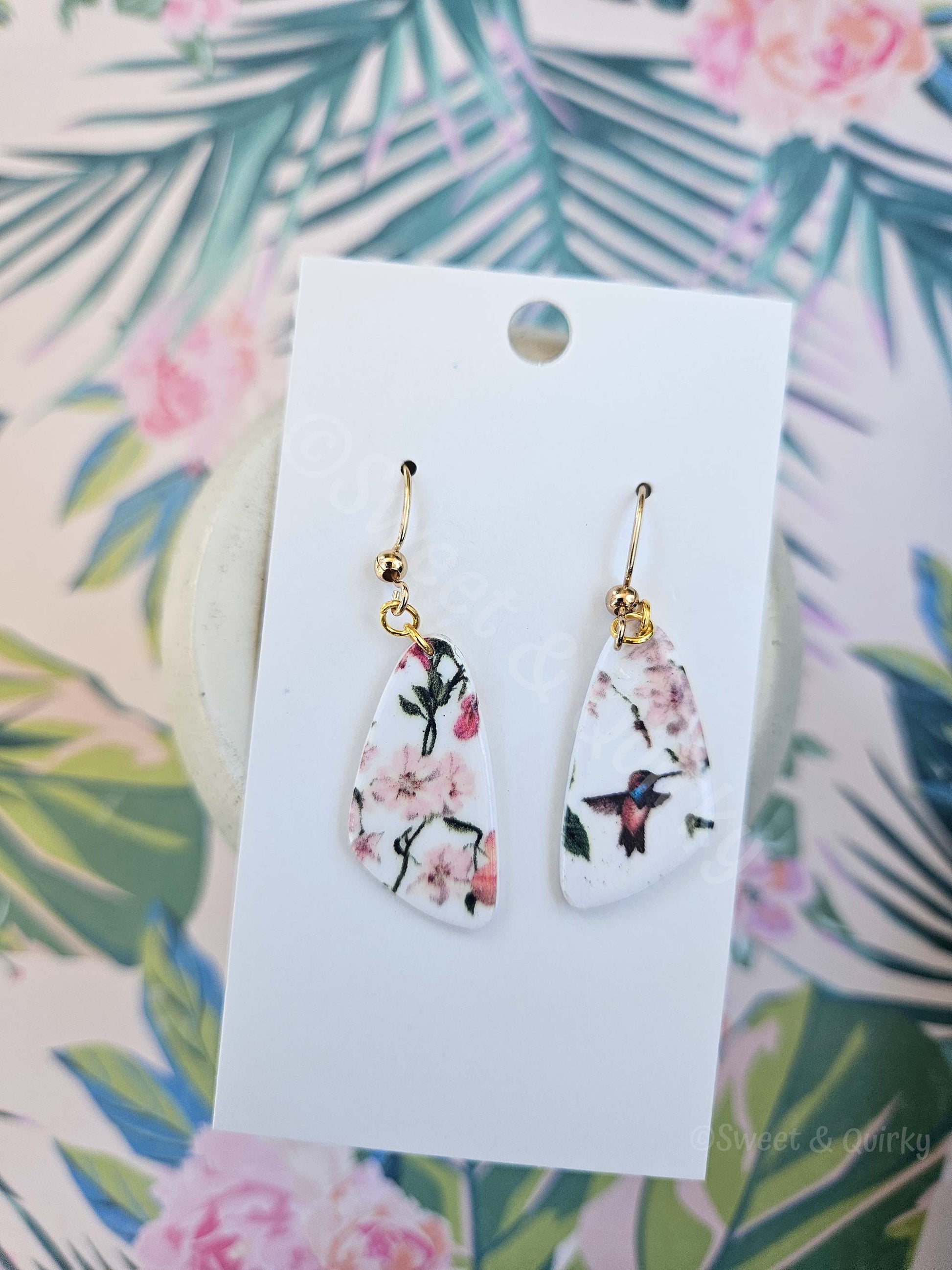 Teardrop-shaped earrings with floral design on a white card against a floral background