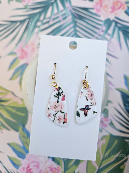 Teardrop-shaped earrings with floral design on a white card against a floral background