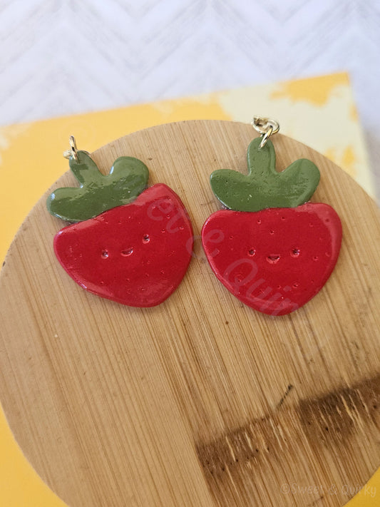 Red strawberry-shaped earrings on a wooden board with a white background