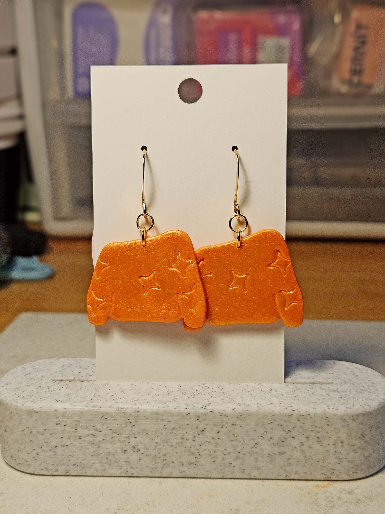 Orange sweater shaped earrings on a white card with a blurred background