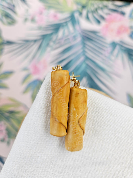 Filipino mini lumpia earrings on a white surface with a floral background