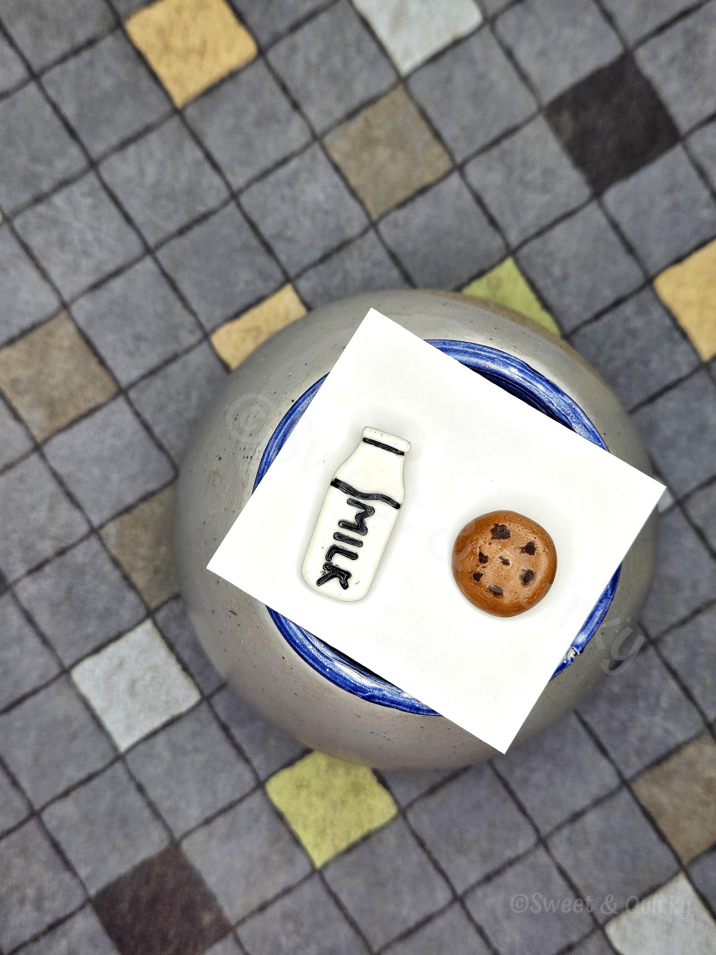 Small cookie and milk bottle stud earings on a white card with a checkered background.
