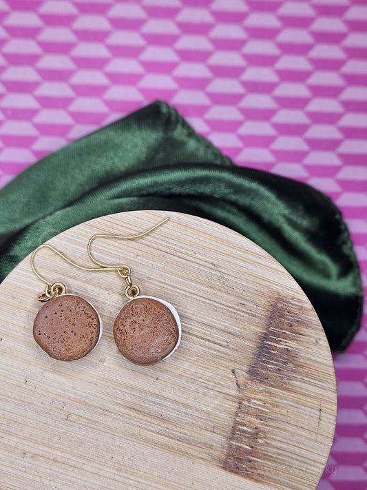 Pair of earrings on a wooden surface with a green fabric and pink geometric patterned background